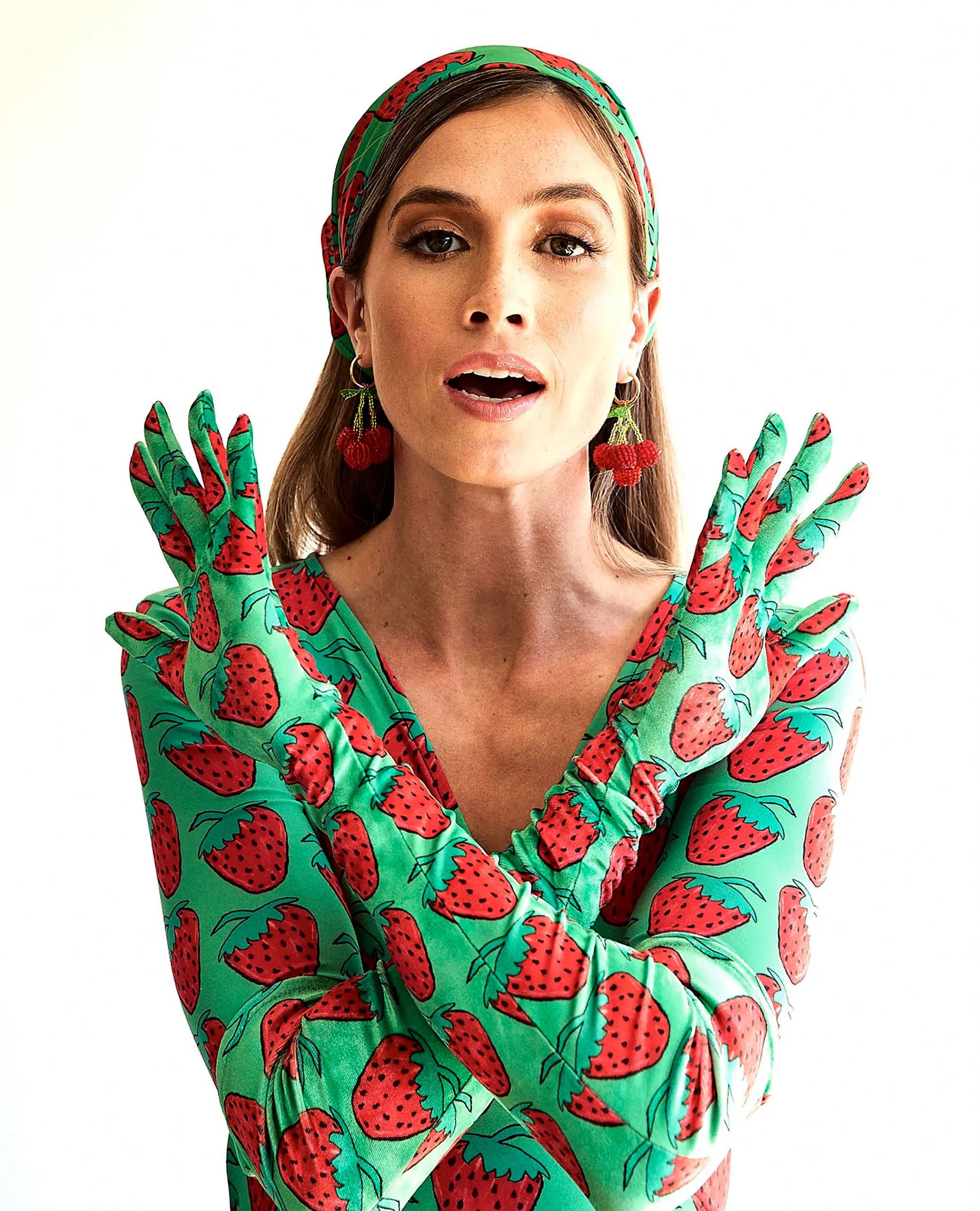 Model wearing red strawberry-print green opera gloves with crossed arms, showing the fingers and long velvet cuffs