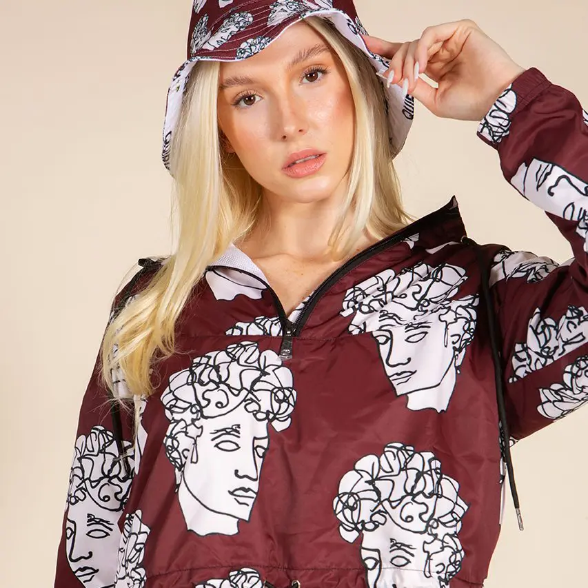 Model wearing Quirk’s burgundy cropped windbreaker with white classical bust illustrations, black half zip and adjustable hem