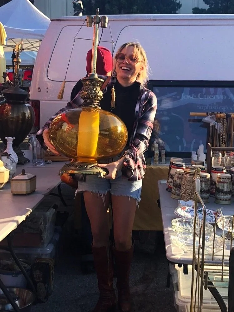 Bridget Connelly holding a vintage amber-and-gold lamp at an outdoor market