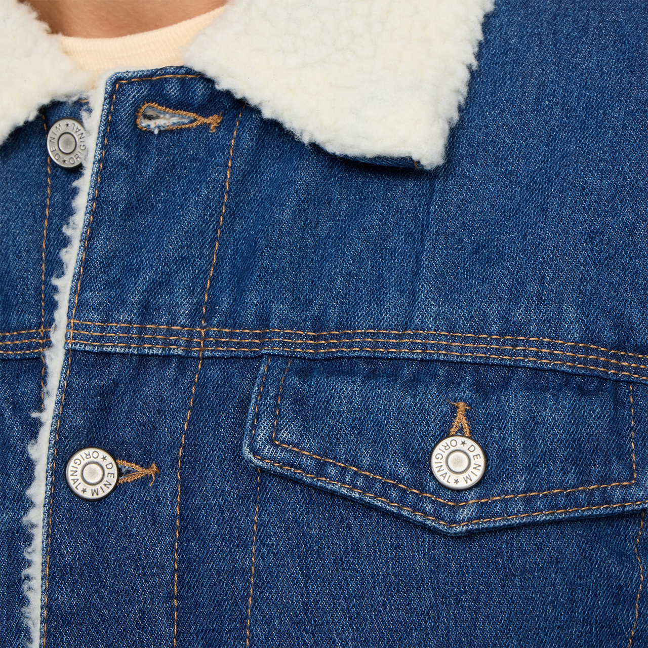 Close view of the PX denim jacket showing its plush contrast collar, metal buttons, chest pocket and stitched seams.