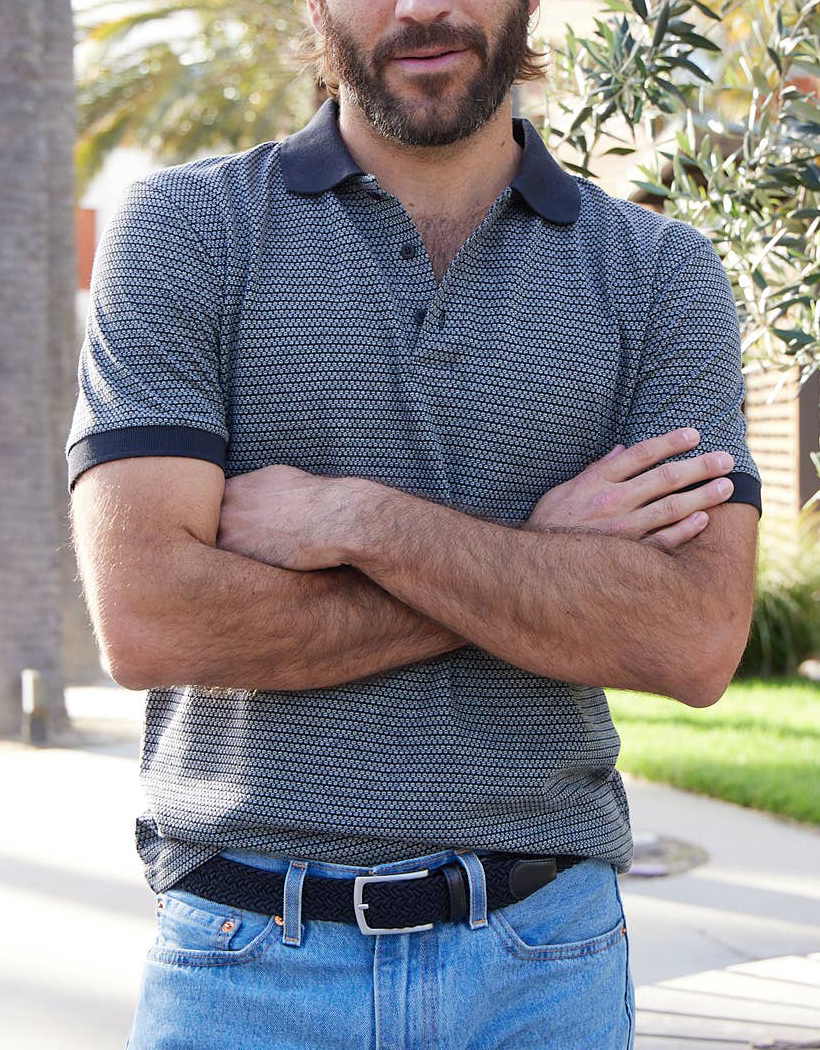 PX black braided belt worn with blue jeans and a navy polo, in a nose-down crop showing the buckle and waist fit.
