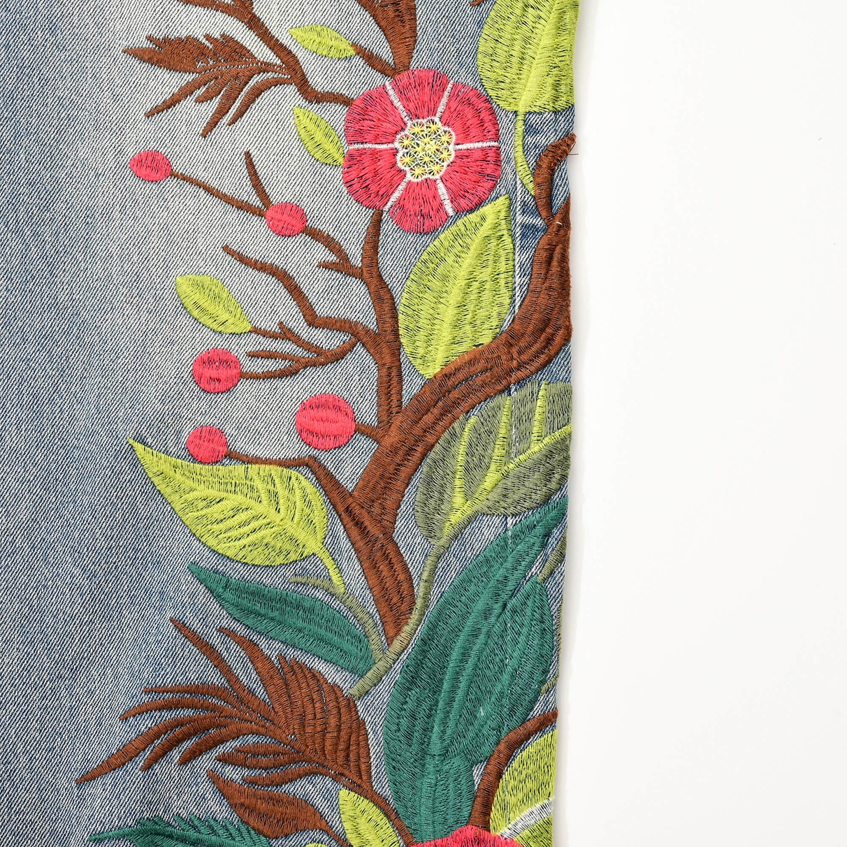 Close view of brown branches, green leaves and pink blossom embroidery beside the outer leg seam.