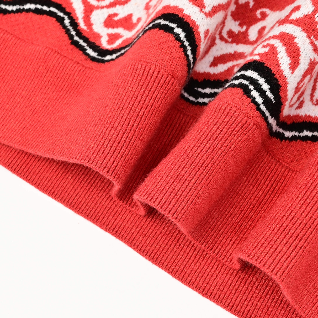 Close view of the coral-red ribbed hem and patterned knit border of the Tiger Rug crewneck
