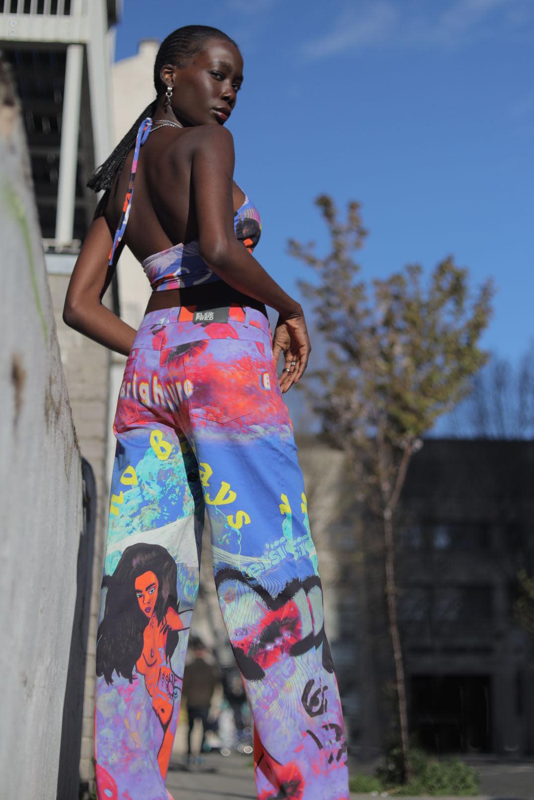 Model wearing Elsie & Fred Brighter Future graphic jeans, showing back patch pockets, the waist label and multicolor illustrated leg panels.