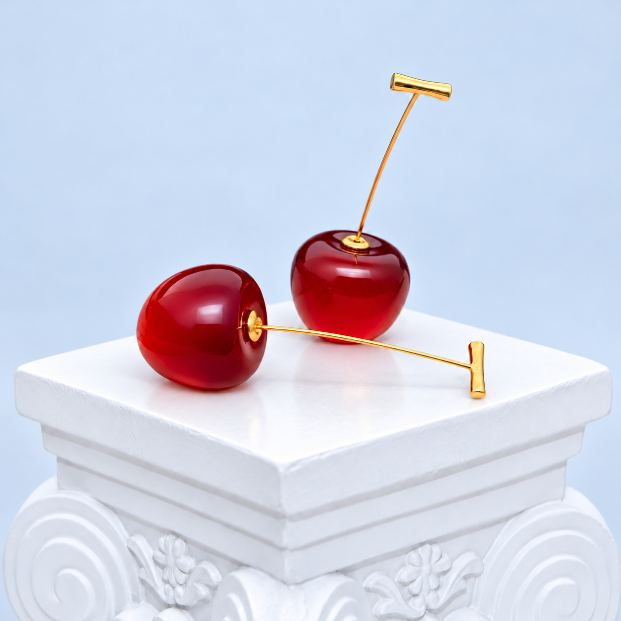 Pair of Mio Queena red resin cherry earrings with fine gold-plated stems and T-bar tops on a white studio pedestal