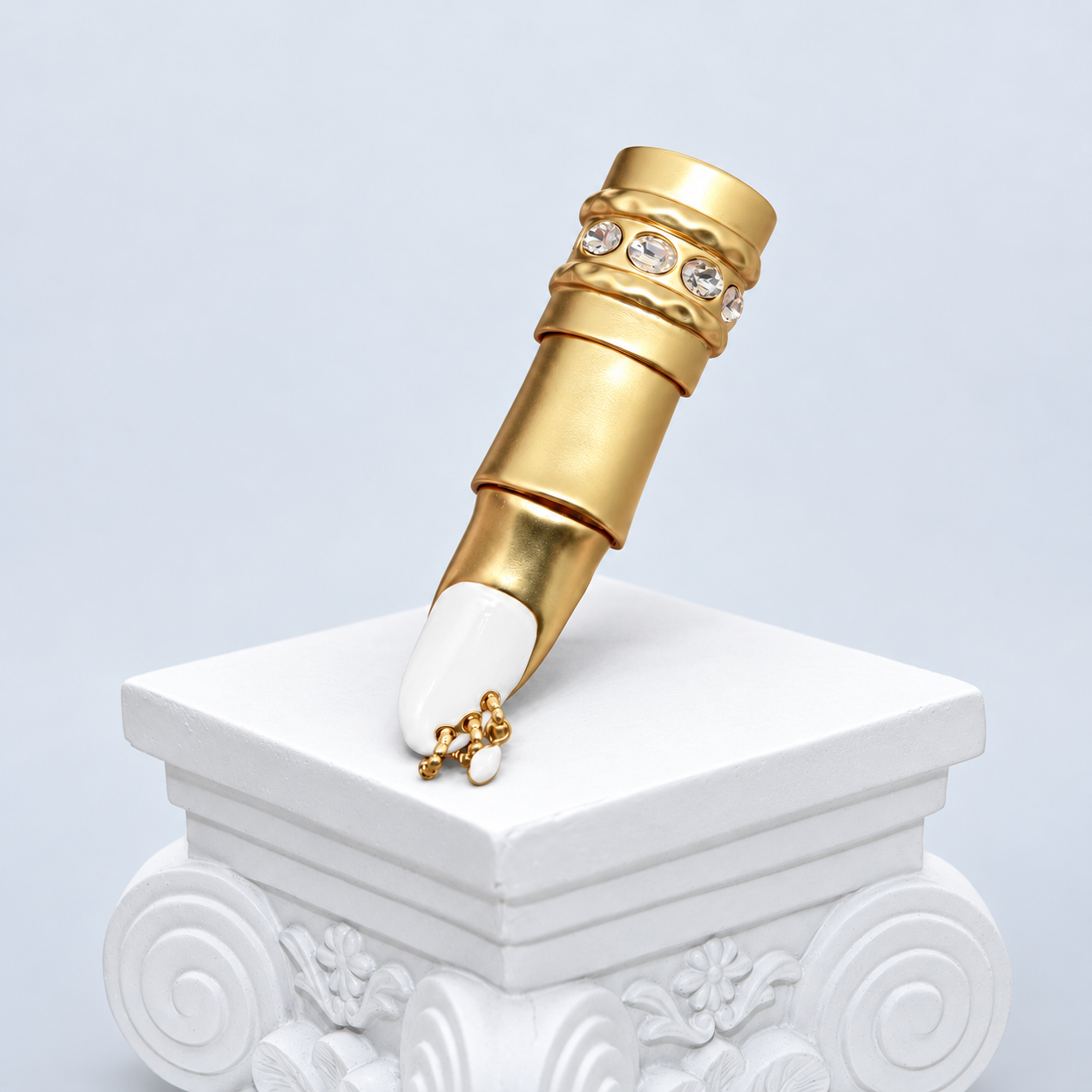 Full front view of the Mio Queena gold-plated articulated finger ring on a white studio pedestal, showing the white enamel nail, clear accents and small chain with one white drop.