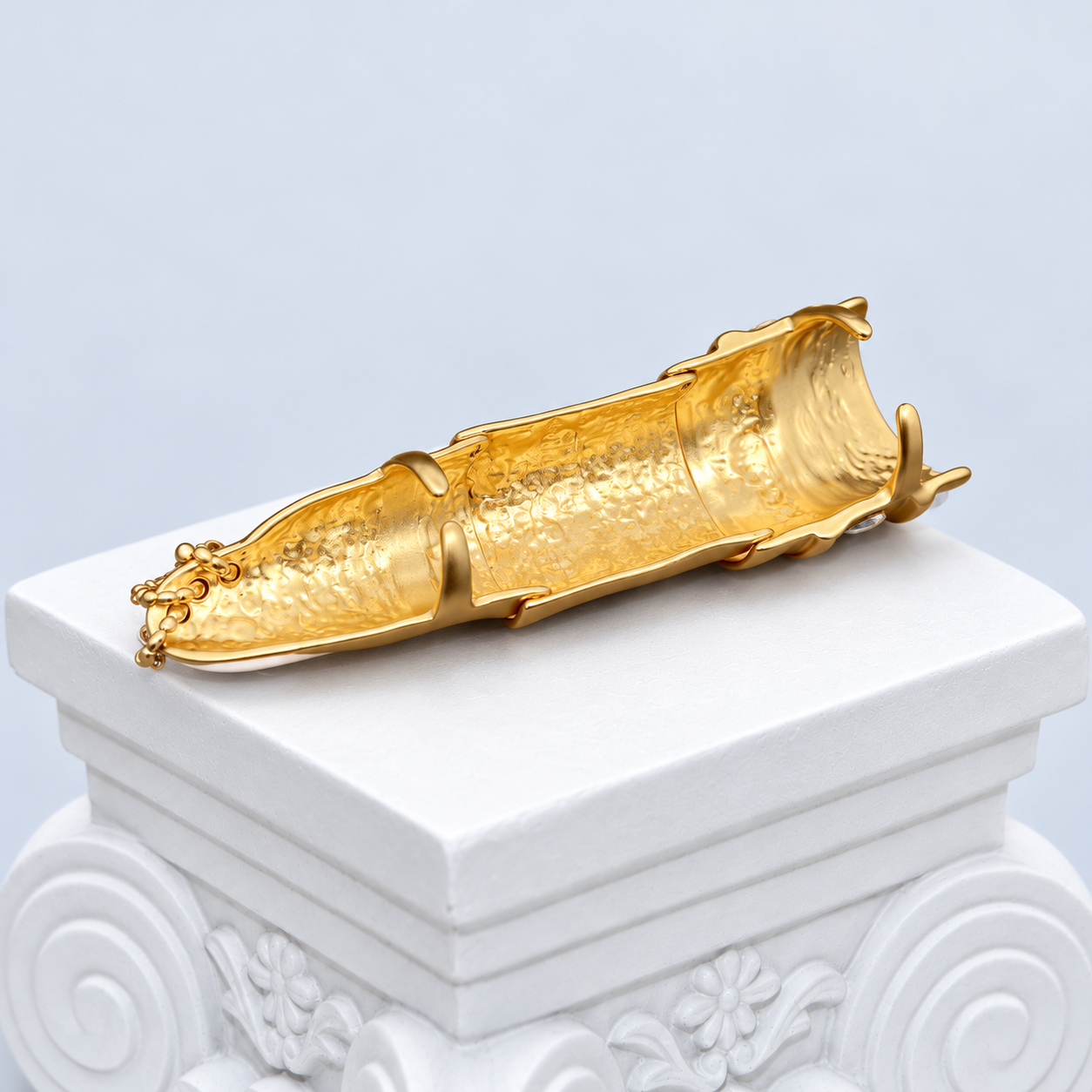 Open underside of the Mio Queena articulated finger ring laid on a white studio pedestal, showing the interior of its overlapping gold-tone sections.