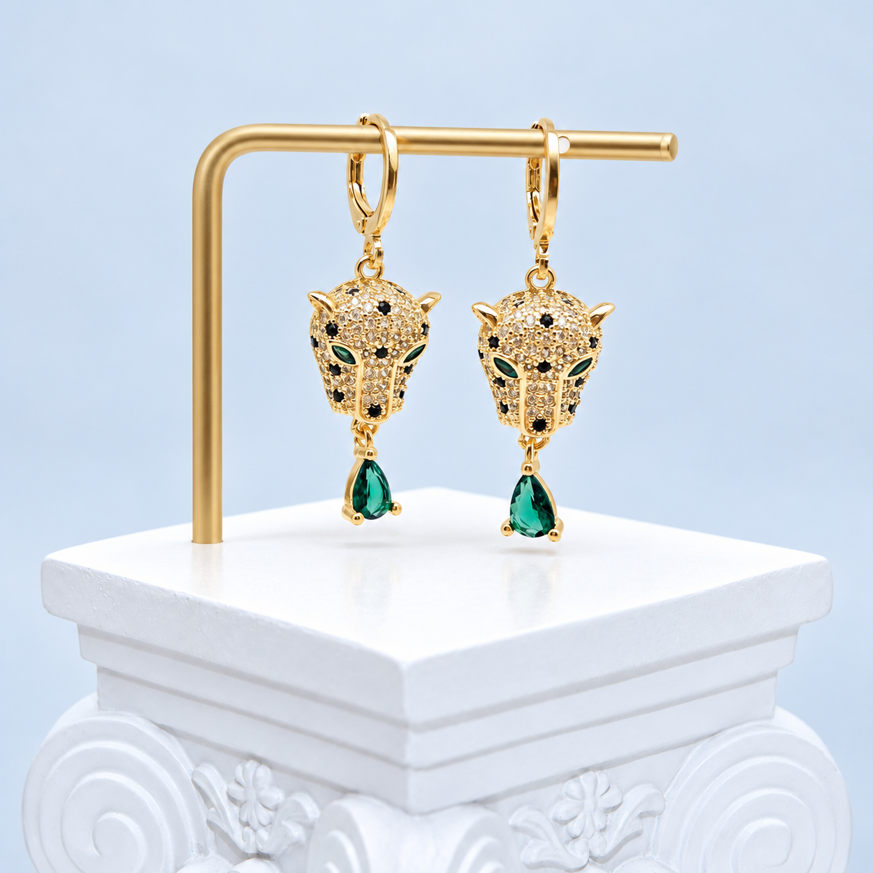 Front view of the Mio Queena gold-plated leopard earrings with green eyes and green teardrop accents on a studio stand